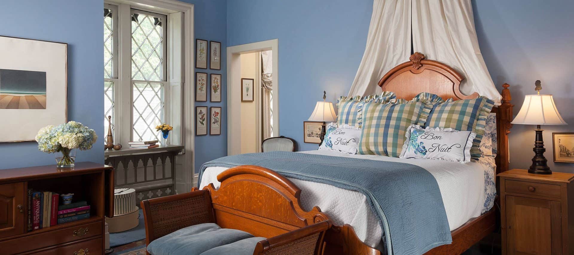 Large bedroom with blue walls, wooden bed, white and blue bedding, wooden loveseat, and wooden cabinet