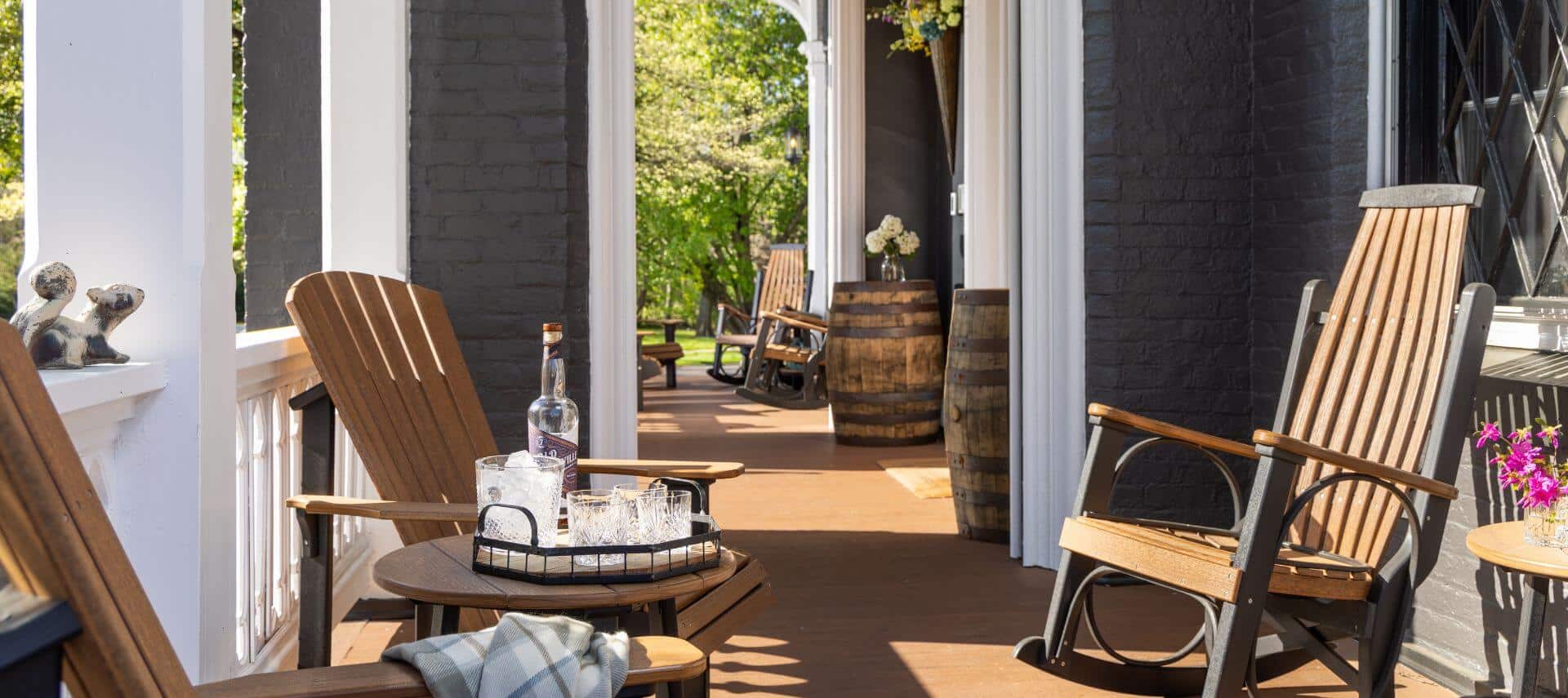 long view of multiple porches with wooden adirondack chairs and rockers at gray house, front porch with wooden stand holding refreshments.