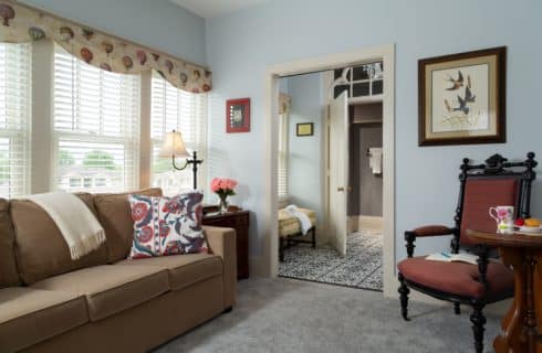 Sitting area with queen sized pull out sofa bed on the left and view of carpeted sitting area transitioning into black and white gothic style tile in the bathroom area.