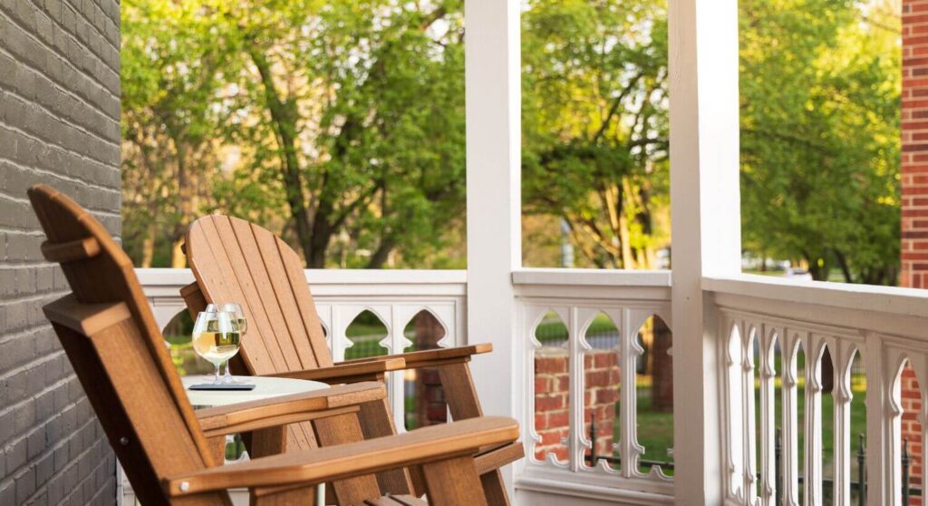 close-up view of 2 wooden adirondack chairs on small porch with white railing, table holding 2 wine glasses