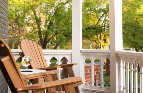 close-up view of 2 wooden adirondack chairs on small porch with white railing, table holding 2 wine glasses