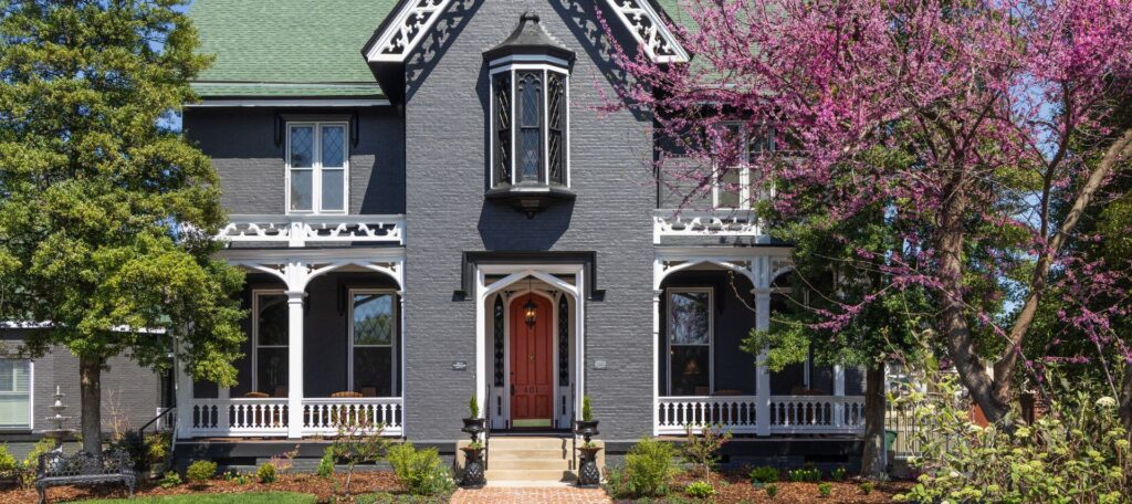 front view of two-story gray house with porches on both sides of landing with red door into house