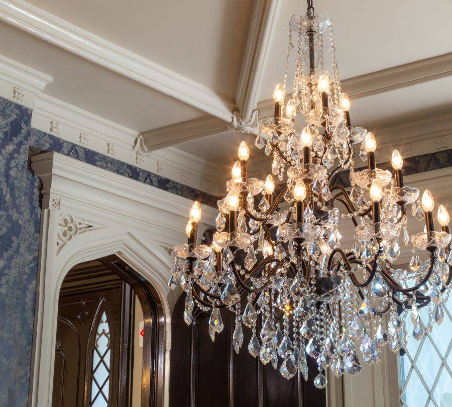 A chandelier hanging down from a tray ceiling of white plaster and ornate doorframe in the background. 