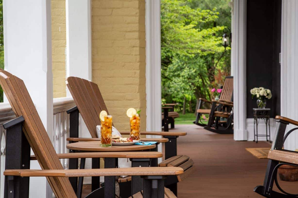 A porch view with two adirondack chairs and two glasses of iced tea with lemon slices on a table between them. 