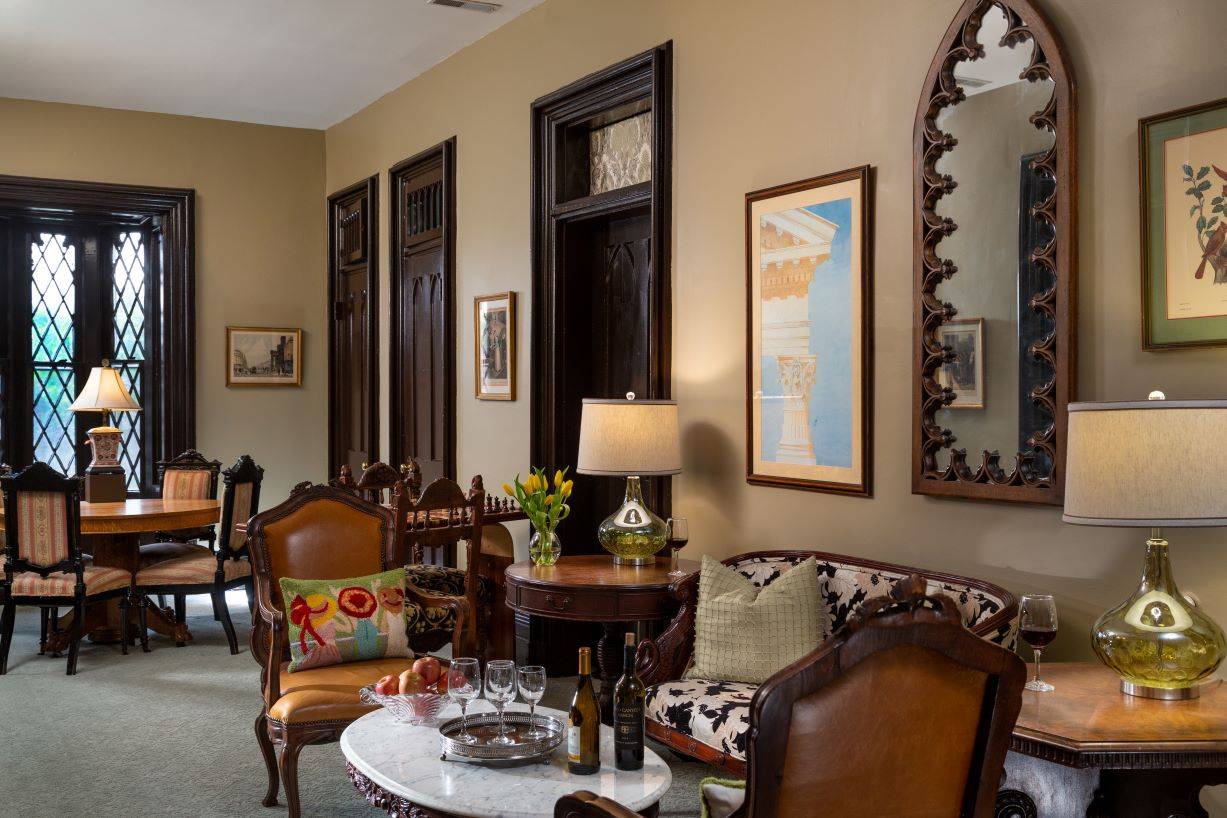 A common area with a setee and two chairs around a marble coffee table, a game table in the background and a large gothic mirror above the loveseat. 