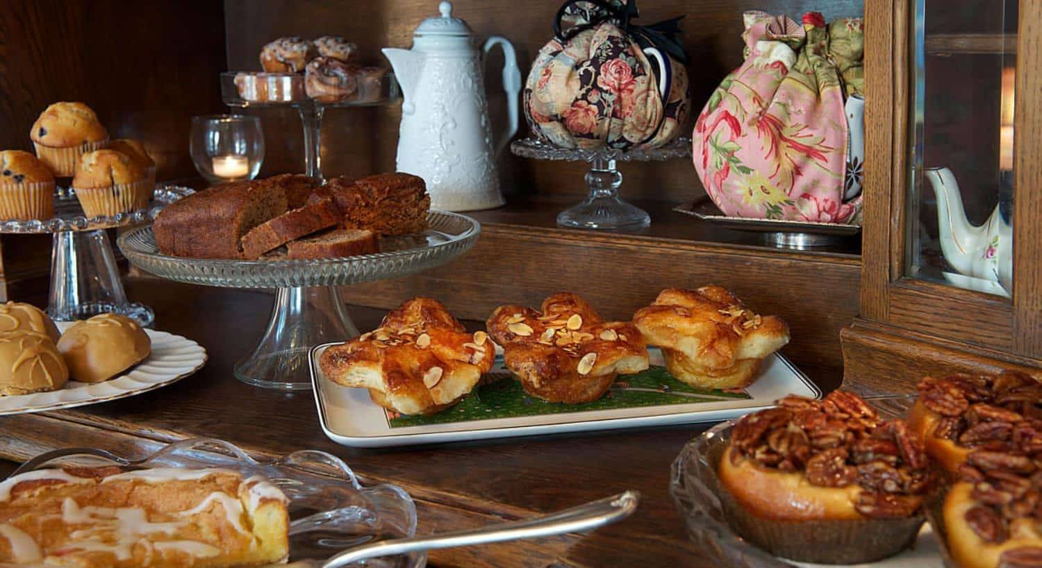 Large assortment of breakfast pastries on glass and porcelain serving dishes on wooden cabinet