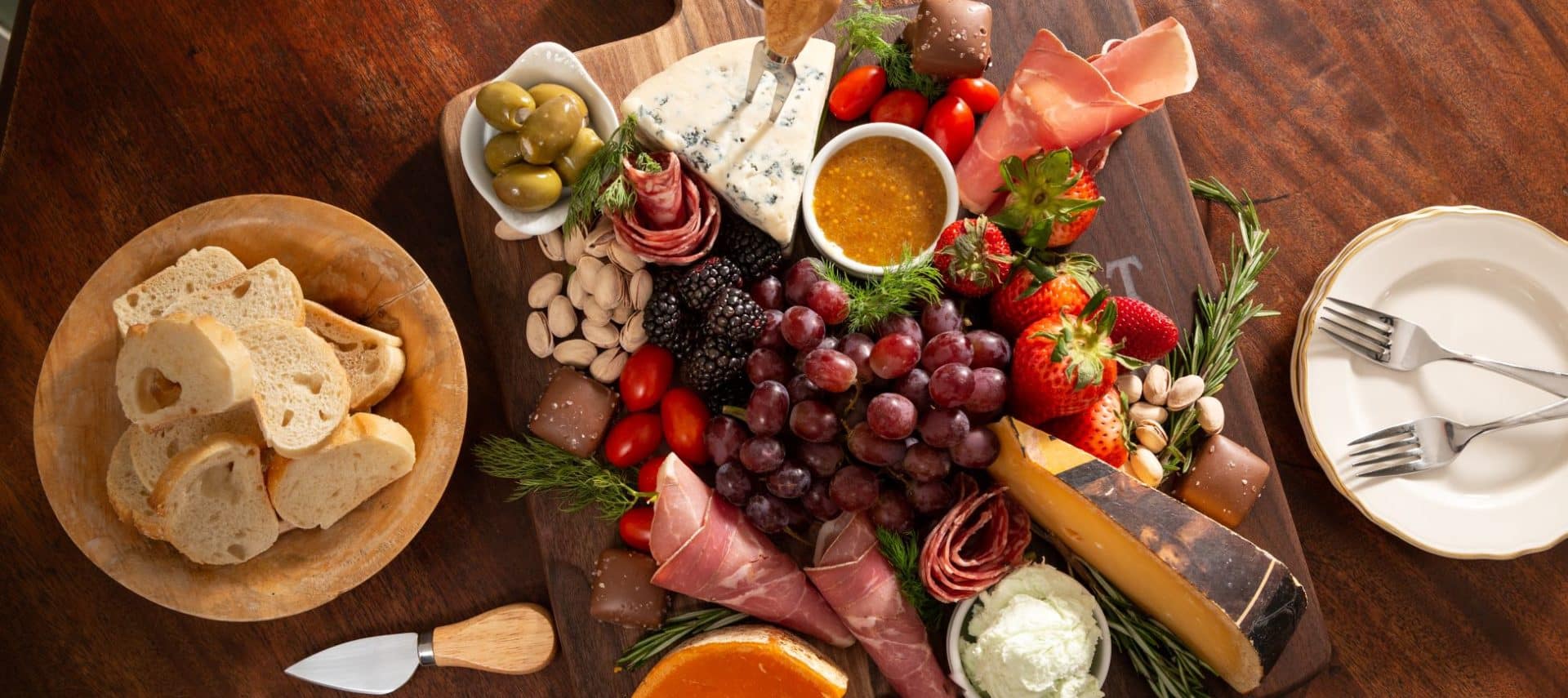 snack board with assorted meats, cheeses, fruits and vegetables with sauces, chocolates and herbs arranged with bread crostinis on the side