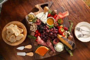 snack board with assorted meats, cheeses, fruits and vegetables with sauces, chocolates and herbs arranged with bread crostinis on the side