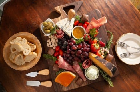 snack board with assorted meats, cheeses, fruits and vegetables with sauces, chocolates and herbs arranged with bread crostinis on the side