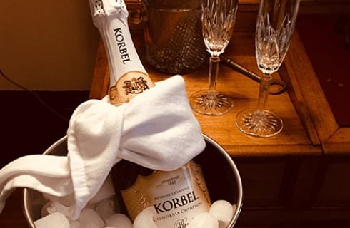 Korbel Champagne chilling in ice bucket with white towel tied around it next to Champagne glasses