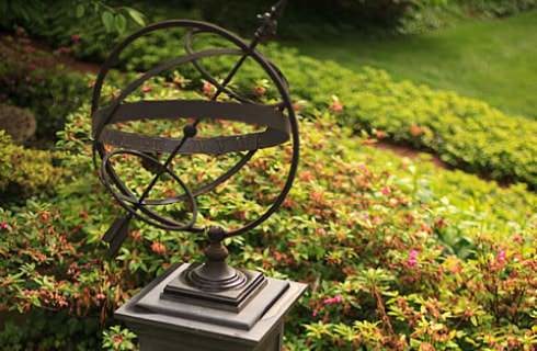 Bronze compass and sun dial statue surrounded by green plants