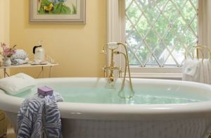 Large white soaker tub, yellow walls, and window with view of green trees outside