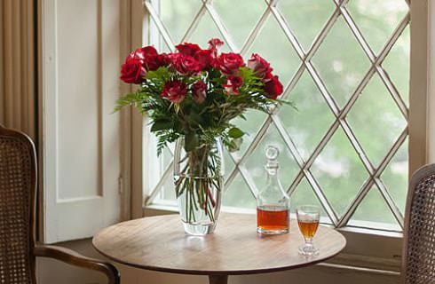 Large glass vase filled with red roses and glass decanter filled with bourbon on small wooden table