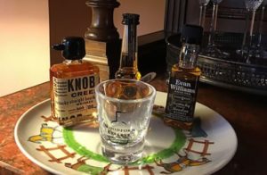 Large plate with different types of bottled bourbon and a shot glass