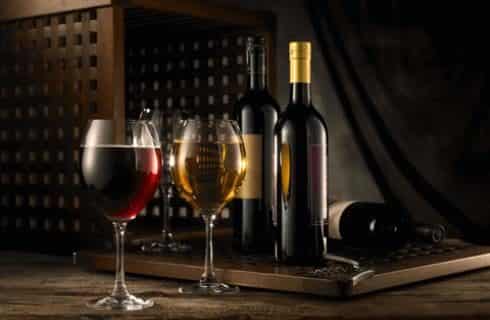 Glass of red wine and glass of white wine on wooden counter next to other wine bottles