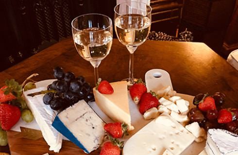 Assortment of cheese and fruit on marble tray and two glasses of white wine sitting on wooden table