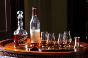 four tasting glasses containing bourbon on a wooden flight board with two bottles of bourbon