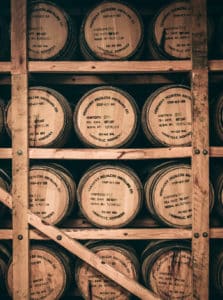 Stacks of three wooden bourbon barrels, stacked four rows high, and stamped with Kentucky Peerless Distillery Co. Louisville, Kentucky.